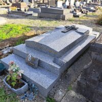monument gris moucheté avec croix posée sur la pierre, et margelle en façade où est posée une plaque avec photo - Natty
