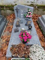 Monument gris moucheté avec stèle sur laquelle figurent 3 photos à côté de l'identification, et à gauche, une croix incrustée garnie de fleurs, espace jardinière en façade - O.Dufour