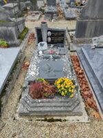 monument en pierre gris avec stèle noire sur laquelle figurent les photos des défunts et leur identité, Sur la pierre tombale une croix, et une plaque avec tête de christ, espace jardinière en façade - O.Dufour