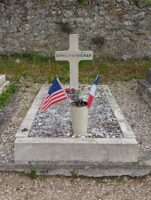Petite tombe entourage pierre et gravillons avec petite croix portant son nom, et dans un vase, un drapeau américain et un drapeau français - Jph Brazier