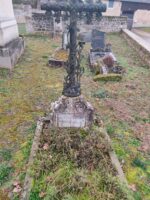 petite tombe entourage pierre, remplie de végétation, avec petite stèle surmontée d'une croix métal ouvragée. Une plaque est fixée sur la petite stèle - O.Dufour