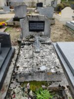 petit monument en pierre avec stèle sur laquelle est fixée une plaque d'identification noire.Crucifix sur la pierre tombale et espace jardinière en façade - O.Dufour