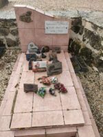 tombe façon carrelage rose avec stèle sur laquelle figure une plaque d'identification et à gauche est fixée une petite maison en métal - O.Dufour