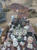 monument marbré bordeaux gris avec de nombreux objets statuettes et plaques. La stèle est de forme arc à gauche - O.Dufour