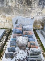 monument gris avec stèle gravée et à gauche de la gravure est fixée une rose noire. nombreuses plaques dont une avec photo