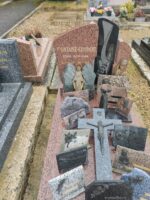 monument moucheté rose et gris avec stèle gravée et traversée par une bande noire avec dessin gris. nombreuses plaques et une croix sur la pierre tombale - O.Dufour