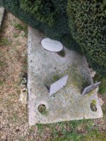 pierre tombale grise, partie supérieure droite couverte par un buisson. au centre plaque d'identification ovale - O.Dufour