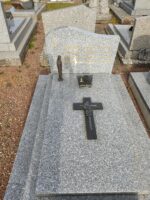 monument gris moucheté avec stèle gravée en lettres dorées et à gauche petite croix. su la pierre tombale, une statuette de vierge à gauche et une croix noire au centre