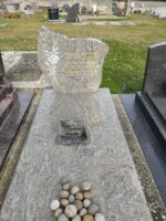 monument gris marbré avec stèle sur laquelle figure une fleur à gauche de l'identification en lettres dorées. sur la pierre tombale des galets - O.Dufour