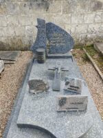 monument gris avec stèle arrondie gravée en lettres dorées. Une urne funéraire parait fixée devant la stèle