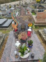 monument couleur gris marbré rose avec stèle arrondie fantaisie sur laquelle figure à côté de l'identification en lettres dorées, une colombe à gauche et à droite 2 hommes et un chien - O.Dufour